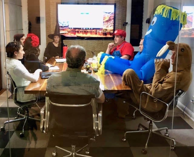 People wearing a variety of Halloween costumes in a conference room.