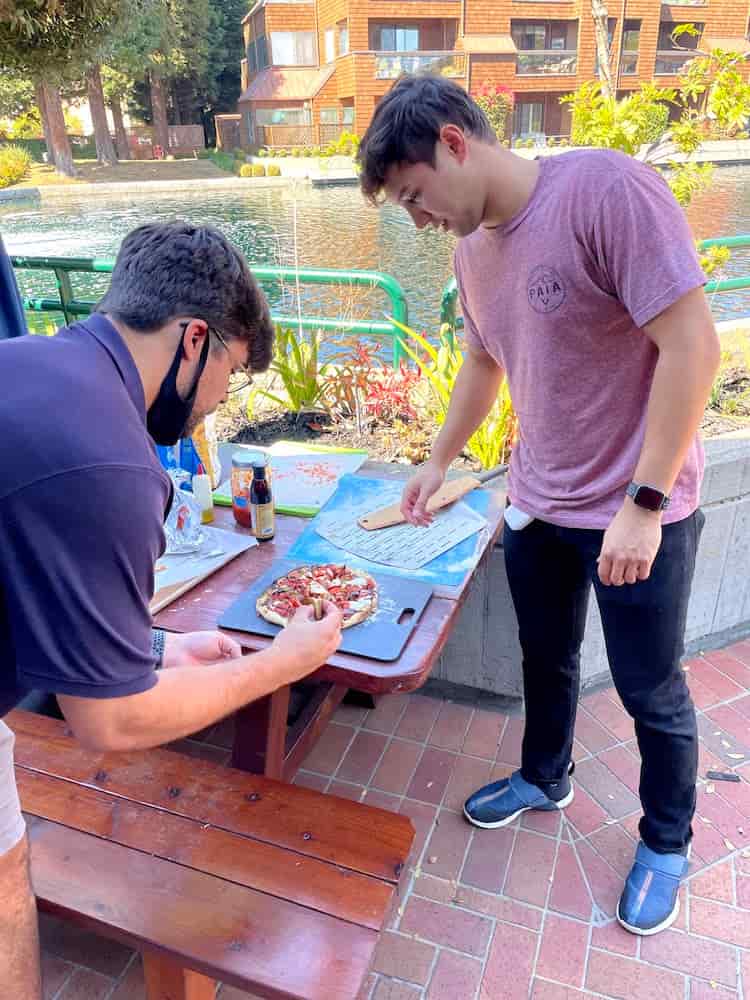 Two people getting a pizza ready for the oven.
