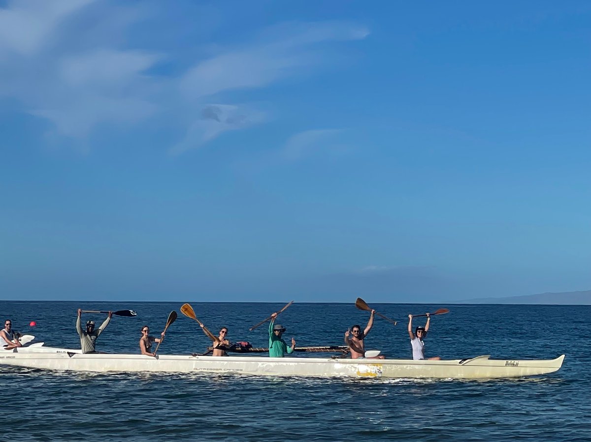 Paddlers in an outrigger canoe in Maui holding their paddles over their heads.