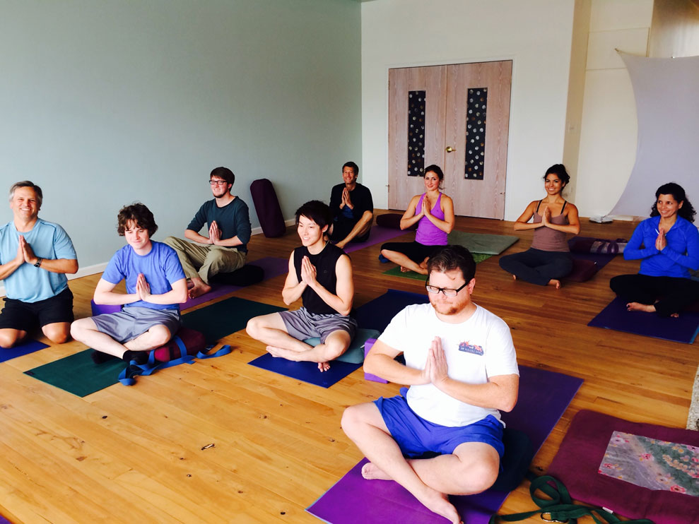 Nine people seated on mats in yoga prayer poses.