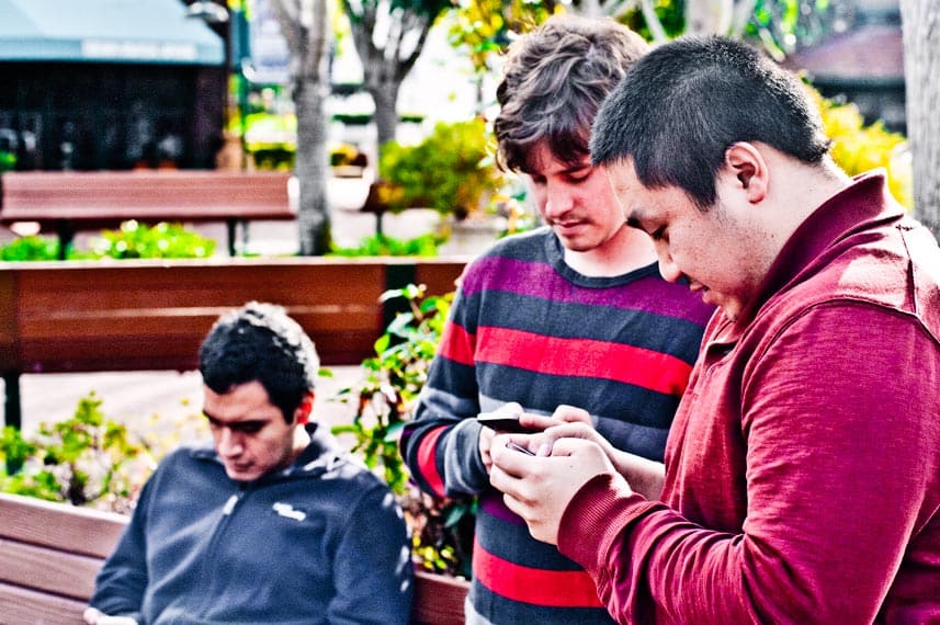 Three people outside all texting on their phones.