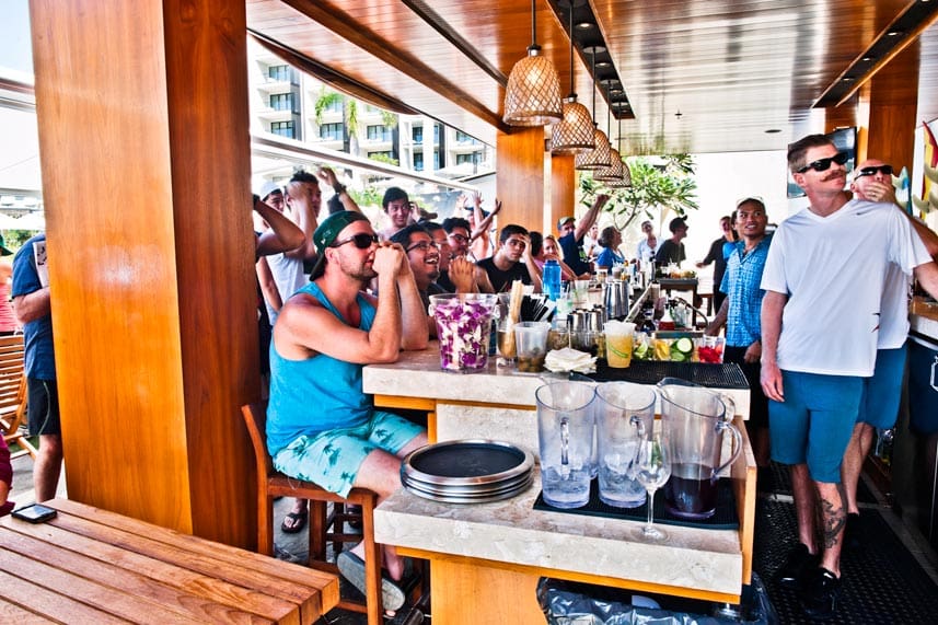 Crowd watching football on TV at a small outdoor bar in Hawaii.