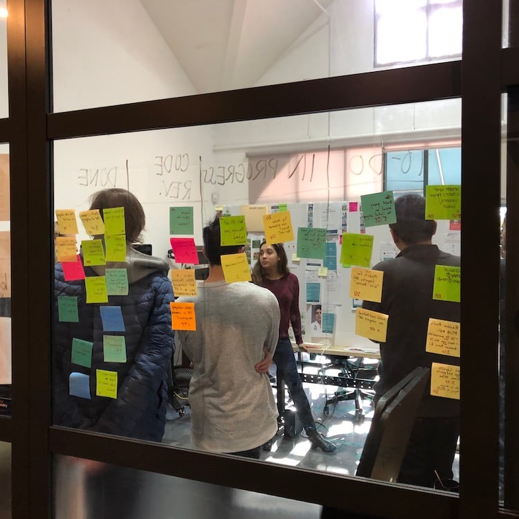 Color-coded sticky notes on a meeting-room glass door.